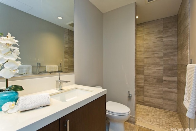 bathroom with vanity, toilet, wood-type flooring, and a tile shower