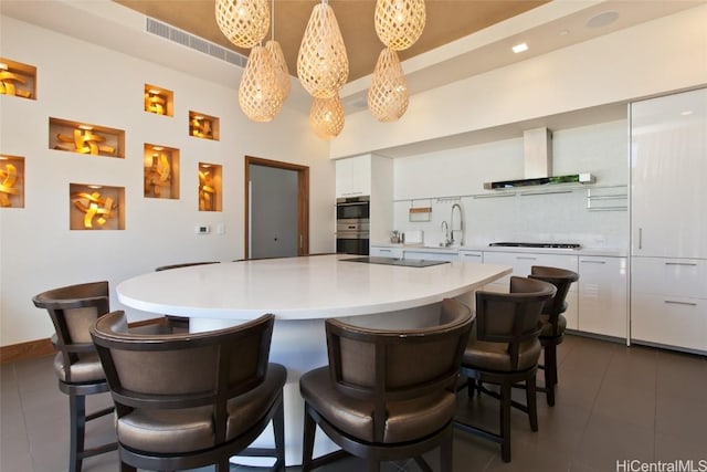 kitchen featuring white cabinetry, pendant lighting, black gas stovetop, and wall chimney exhaust hood