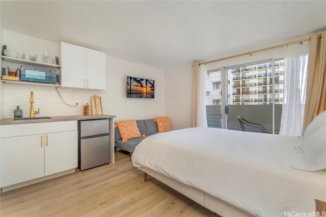 bedroom featuring sink, light hardwood / wood-style flooring, stainless steel refrigerator, and access to exterior