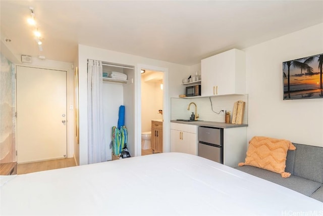 bedroom with sink, hardwood / wood-style flooring, fridge, connected bathroom, and a closet