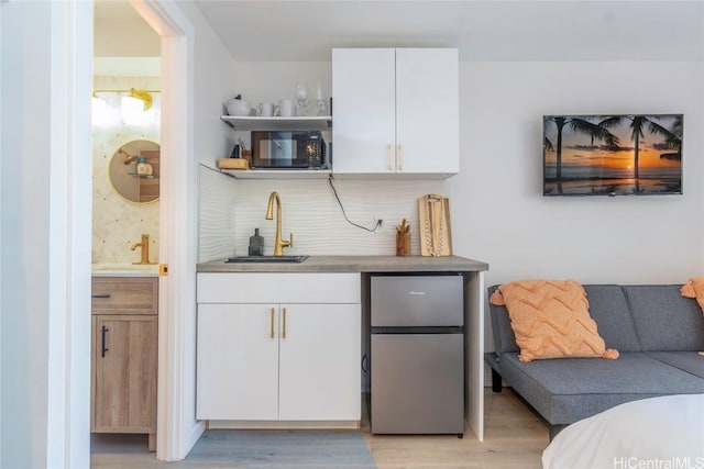 bar with white cabinetry, sink, stainless steel fridge, and light hardwood / wood-style flooring