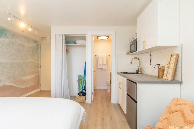 bedroom featuring sink, ensuite bath, stainless steel refrigerator, light hardwood / wood-style floors, and a closet