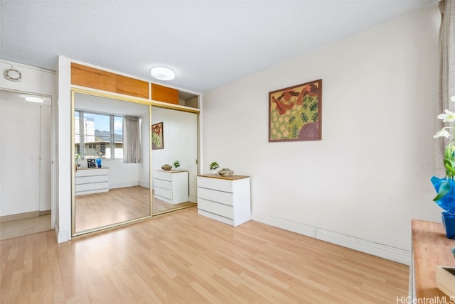 unfurnished bedroom with a textured ceiling, a closet, wood finished floors, and baseboards