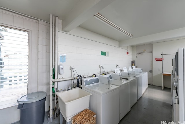 community laundry room featuring concrete block wall, a sink, and washing machine and clothes dryer