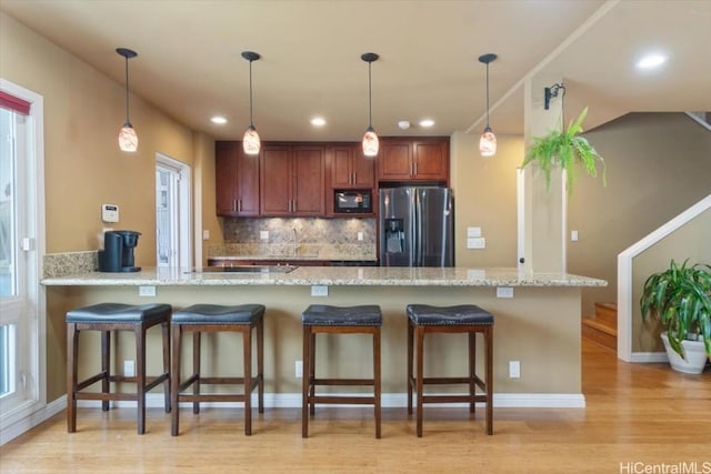 kitchen with stainless steel fridge, kitchen peninsula, light stone countertops, and backsplash