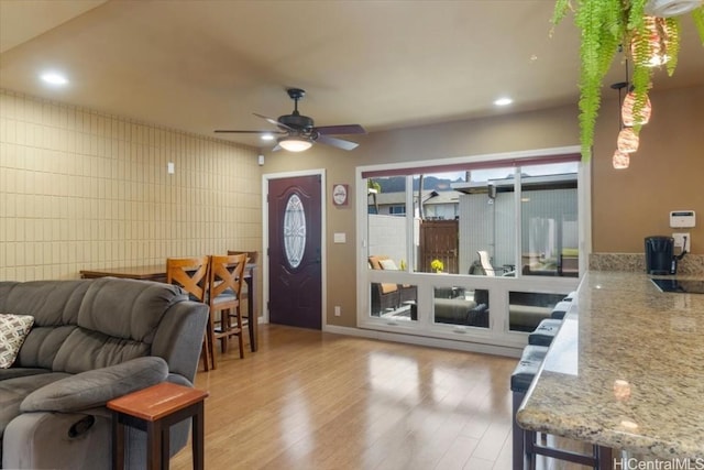 living room with ceiling fan, light hardwood / wood-style floors, and tile walls