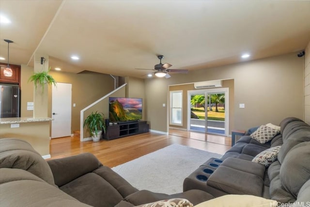 living room with a wall unit AC, ceiling fan, and light wood-type flooring