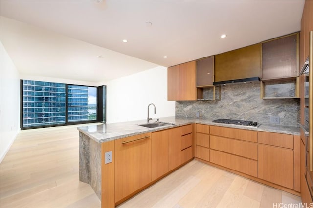 kitchen featuring stainless steel gas cooktop, sink, light hardwood / wood-style flooring, kitchen peninsula, and light stone countertops