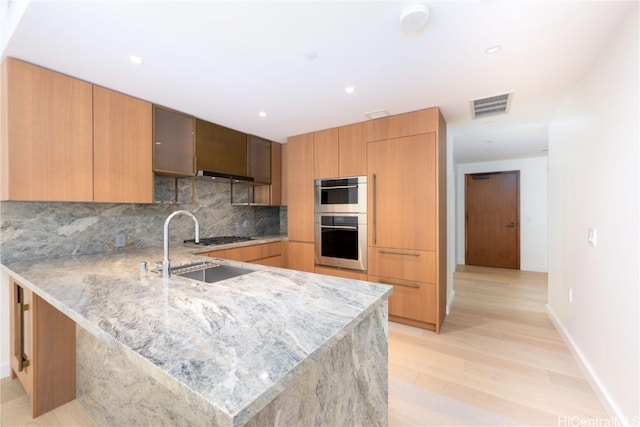 kitchen featuring appliances with stainless steel finishes, decorative backsplash, light stone counters, and kitchen peninsula