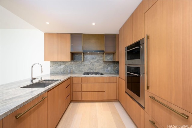 kitchen featuring sink, backsplash, light hardwood / wood-style floors, stainless steel appliances, and light stone countertops