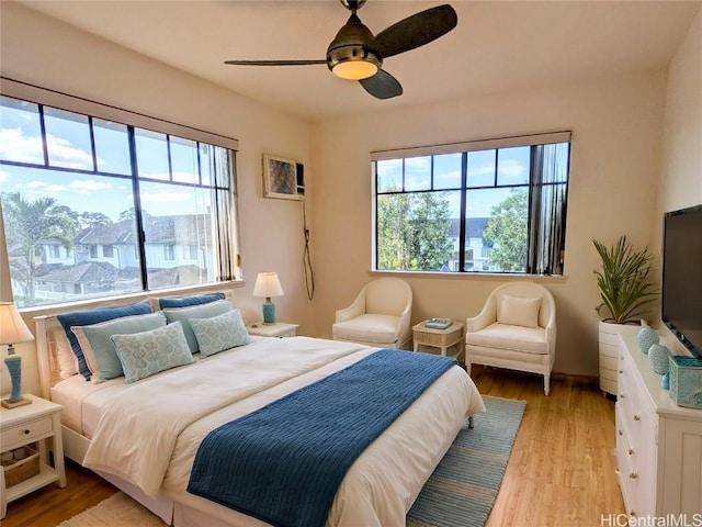 bedroom with ceiling fan, a wall mounted air conditioner, multiple windows, and light wood-type flooring