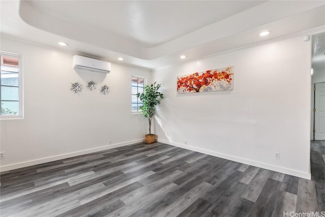 empty room featuring dark wood-type flooring, a wall mounted air conditioner, and a tray ceiling