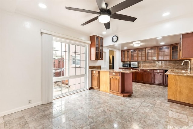 kitchen featuring sink, kitchen peninsula, ceiling fan, light stone countertops, and decorative backsplash