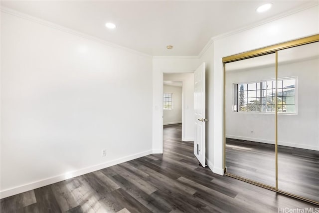 unfurnished bedroom with multiple windows, ornamental molding, dark wood-type flooring, and a closet