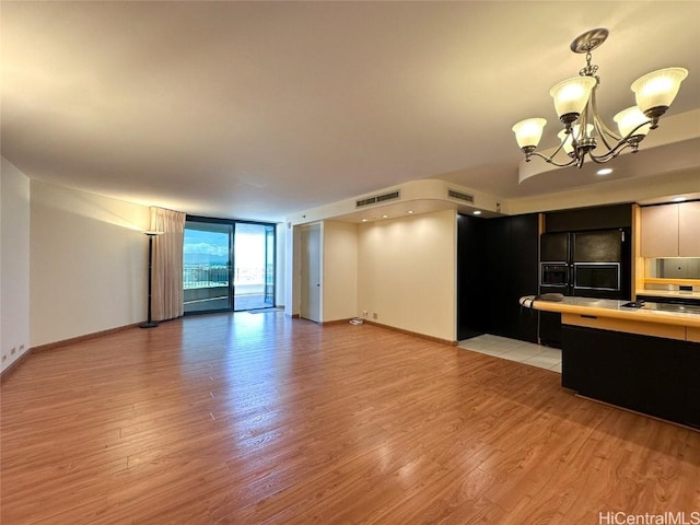 unfurnished living room with an inviting chandelier, light hardwood / wood-style flooring, and a wall of windows