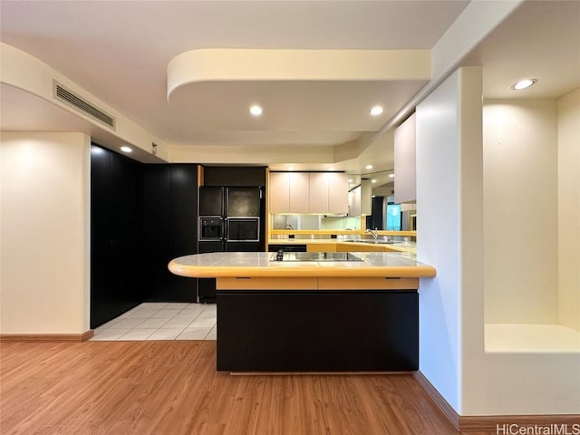 kitchen featuring kitchen peninsula, light hardwood / wood-style floors, white cabinetry, and black appliances