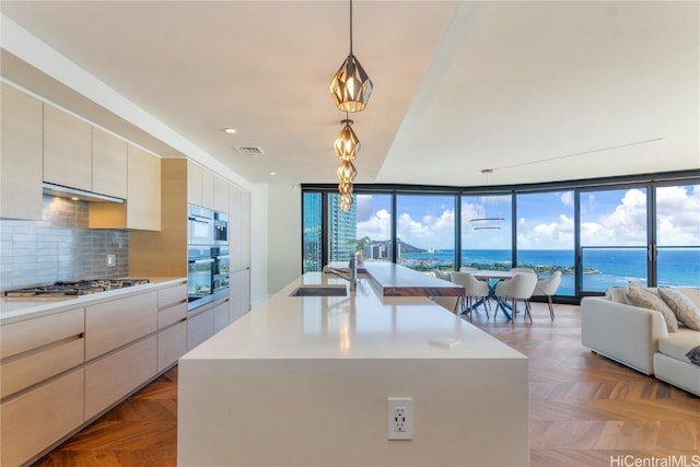 kitchen with sink, a water view, decorative light fixtures, appliances with stainless steel finishes, and a kitchen island with sink