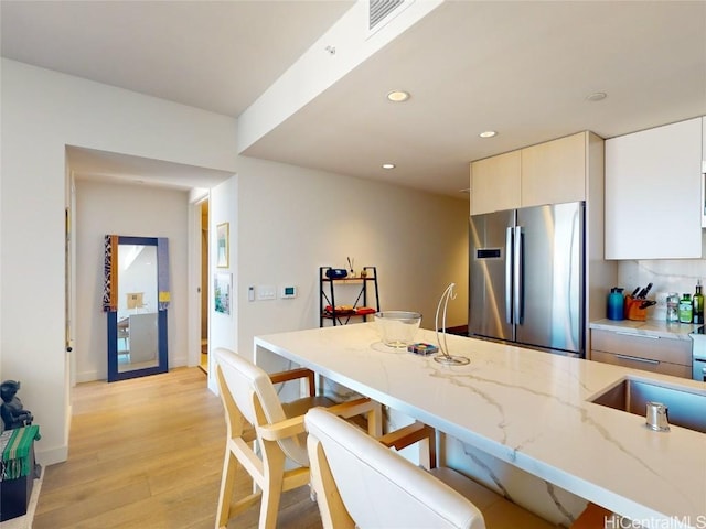 kitchen with stainless steel refrigerator, white cabinetry, sink, light stone counters, and light wood-type flooring