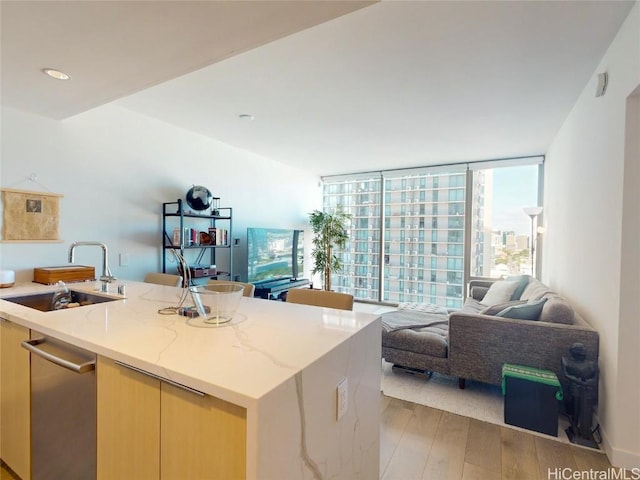 kitchen featuring sink, expansive windows, light stone countertops, a center island with sink, and light wood-type flooring