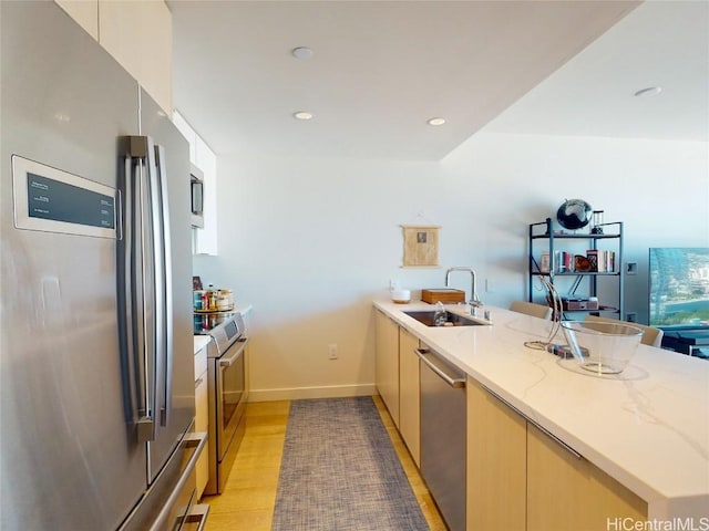 kitchen with sink, appliances with stainless steel finishes, light stone counters, light hardwood / wood-style floors, and kitchen peninsula