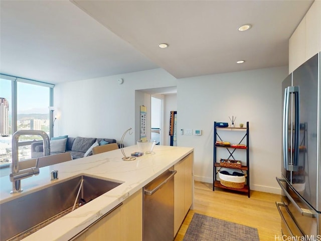 kitchen featuring stainless steel appliances, sink, light stone counters, and light hardwood / wood-style floors