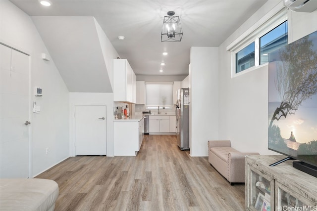 kitchen featuring pendant lighting, stainless steel refrigerator, white cabinets, an inviting chandelier, and light hardwood / wood-style flooring