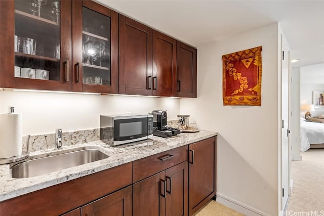 kitchen with light stone countertops, sink, light carpet, and dark brown cabinets