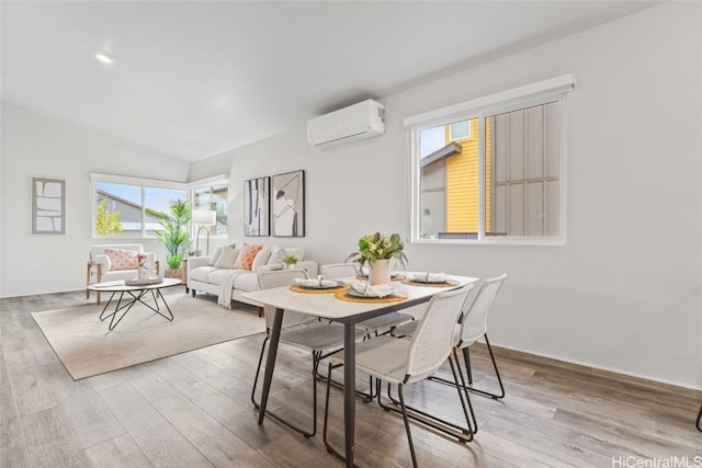 dining room with lofted ceiling, plenty of natural light, a wall mounted AC, and light wood-type flooring