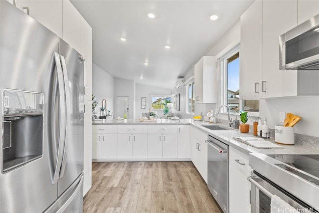 kitchen featuring sink, light hardwood / wood-style flooring, appliances with stainless steel finishes, white cabinetry, and vaulted ceiling