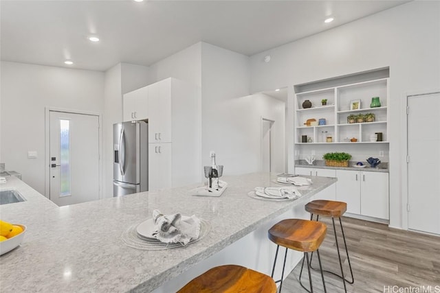 kitchen with white cabinetry, a kitchen bar, stainless steel fridge, and light hardwood / wood-style flooring