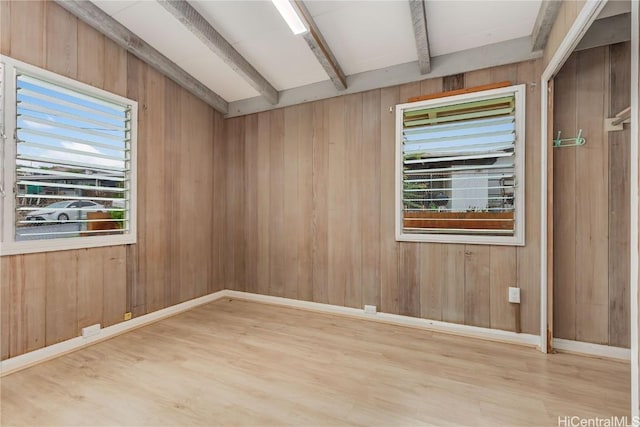 spare room featuring plenty of natural light, beam ceiling, wood-type flooring, and wood walls