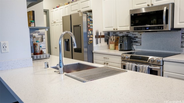 kitchen with sink, white cabinets, decorative backsplash, stainless steel appliances, and light stone countertops