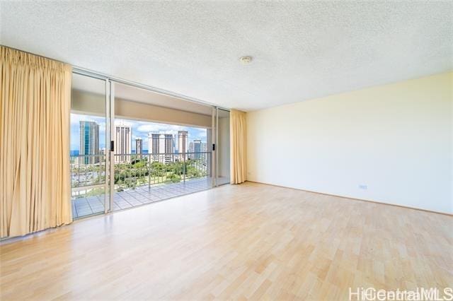 empty room featuring a wall of windows, wood-type flooring, and a textured ceiling