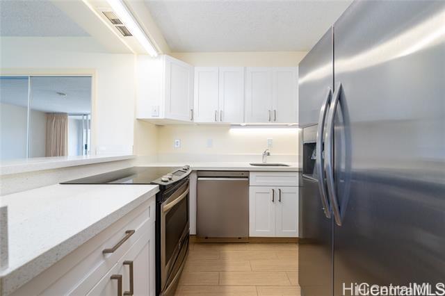 kitchen with appliances with stainless steel finishes, sink, white cabinets, light stone counters, and light hardwood / wood-style flooring