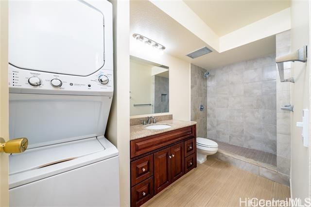 bathroom featuring stacked washer and dryer, hardwood / wood-style flooring, vanity, a tile shower, and toilet