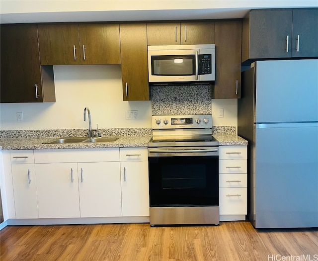 kitchen with light stone counters, sink, light hardwood / wood-style floors, and appliances with stainless steel finishes