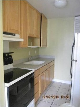 kitchen featuring light tile patterned flooring, sink, light brown cabinets, white refrigerator, and electric range