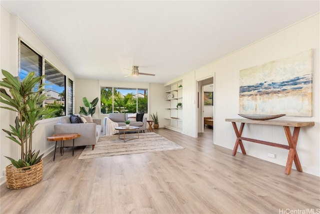 living room with built in features, ceiling fan, and light wood-type flooring