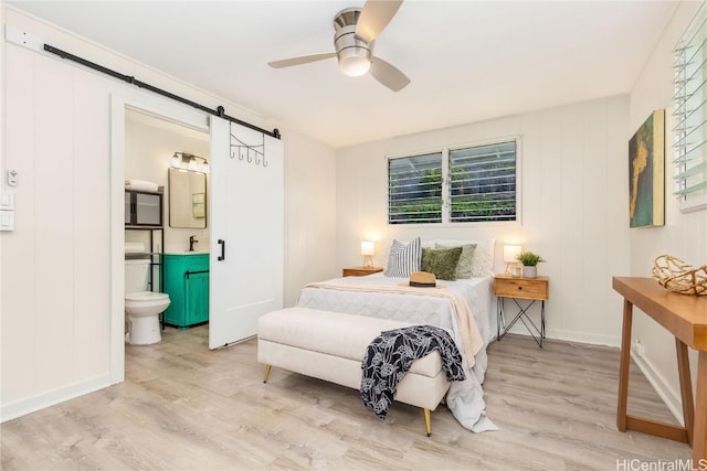 bedroom with connected bathroom, sink, ceiling fan, a barn door, and light wood-type flooring