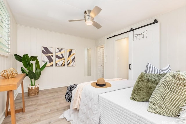 bedroom with hardwood / wood-style flooring, ceiling fan, and a barn door