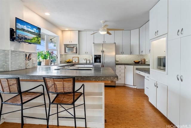 kitchen with stainless steel refrigerator with ice dispenser, a kitchen bar, kitchen peninsula, and white cabinets