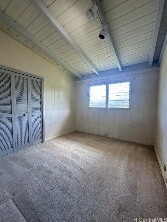 unfurnished bedroom featuring vaulted ceiling with beams and carpet