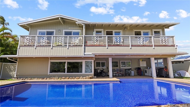 rear view of property with an outdoor pool, a balcony, and a patio