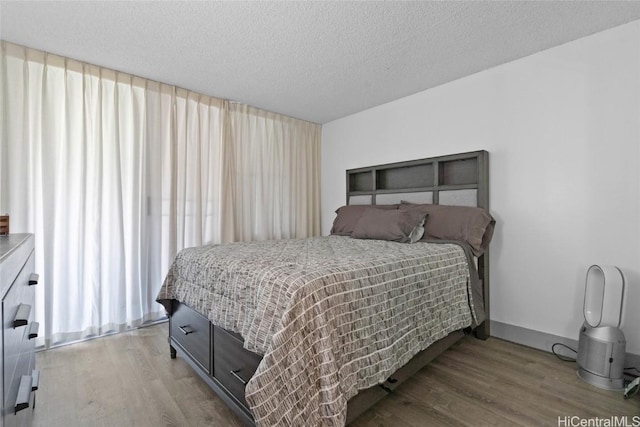 bedroom with a textured ceiling, baseboards, and wood finished floors