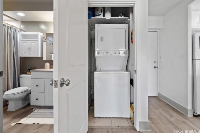 laundry room with laundry area, baseboards, light wood finished floors, and stacked washer / drying machine