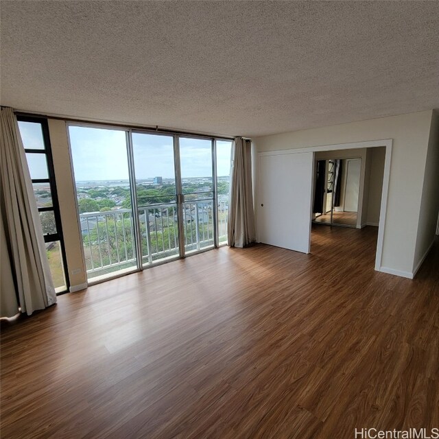 unfurnished room with expansive windows, dark wood-type flooring, and a textured ceiling