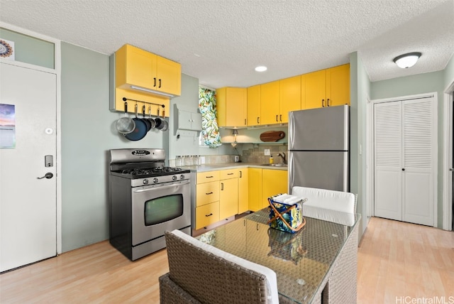 kitchen with appliances with stainless steel finishes, a textured ceiling, and light hardwood / wood-style flooring