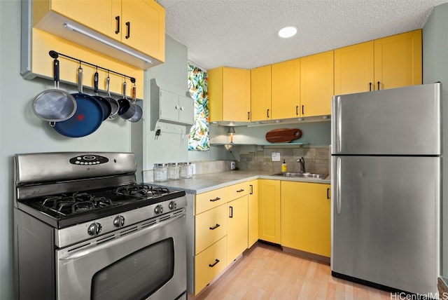 kitchen featuring sink, a textured ceiling, light wood-type flooring, stainless steel appliances, and backsplash