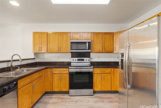 kitchen with stainless steel appliances, sink, dark stone counters, and light hardwood / wood-style flooring