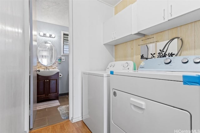 clothes washing area featuring independent washer and dryer, sink, cabinets, and light wood-type flooring